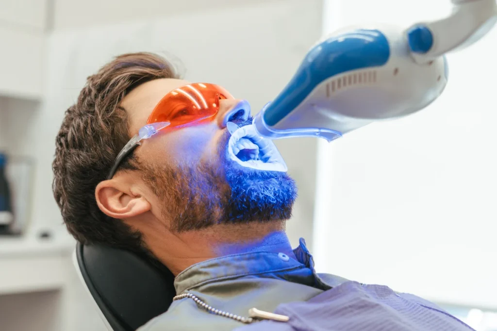 Dentist performing professional teeth whitening treatment using a dental light while the patient wears protective eyewear